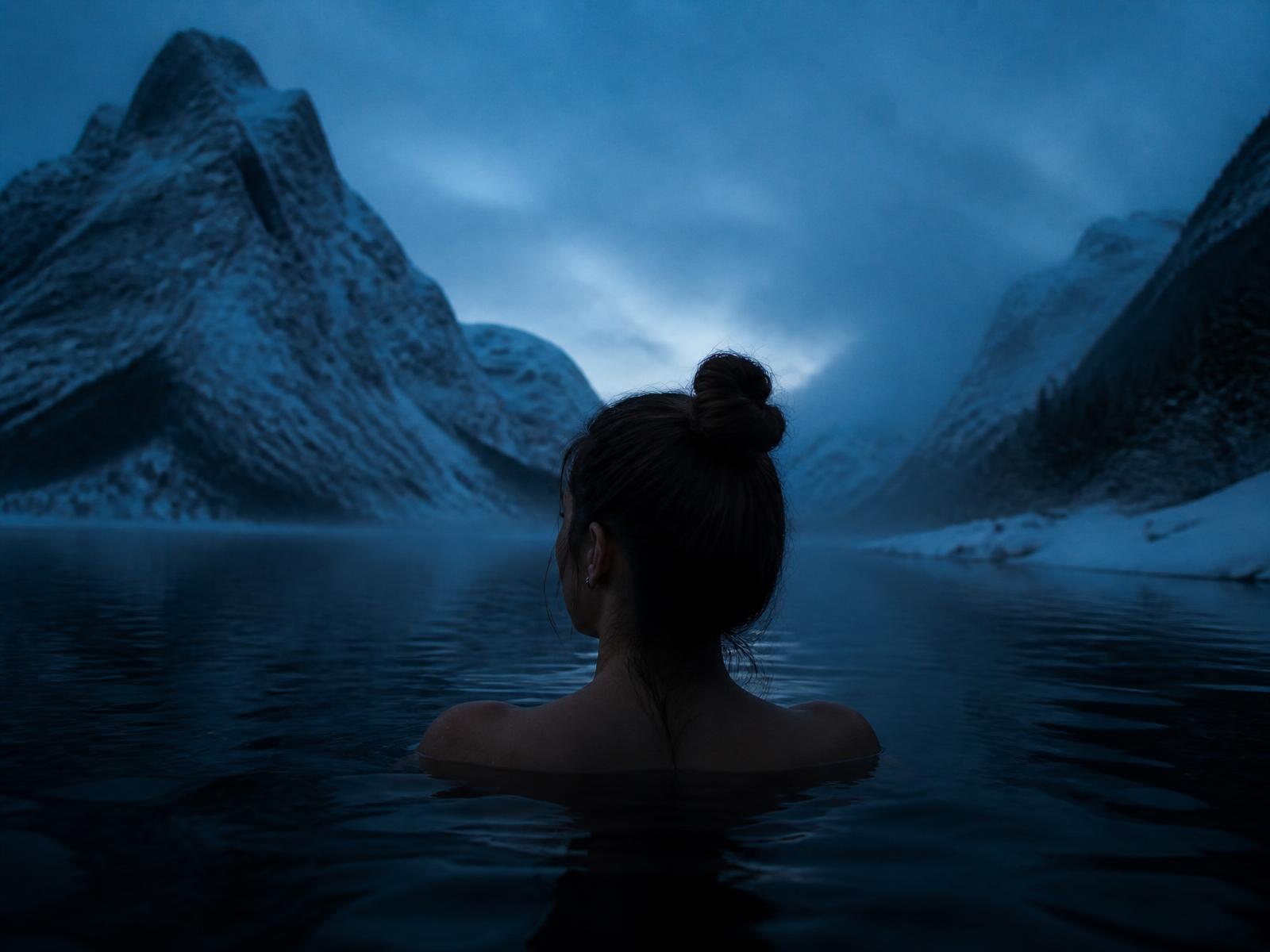 A woman immersed to the shoulders in a dark glacial lake at blue hour